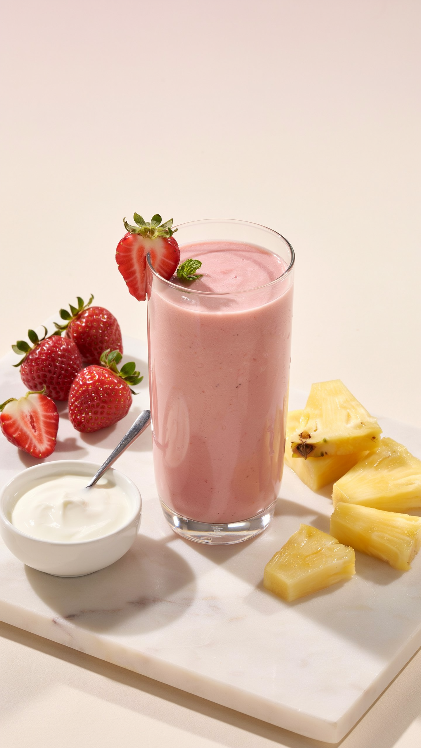 Strawberry pineapple yogurt smoothie in a glass with a honey drizzle and fresh fruit