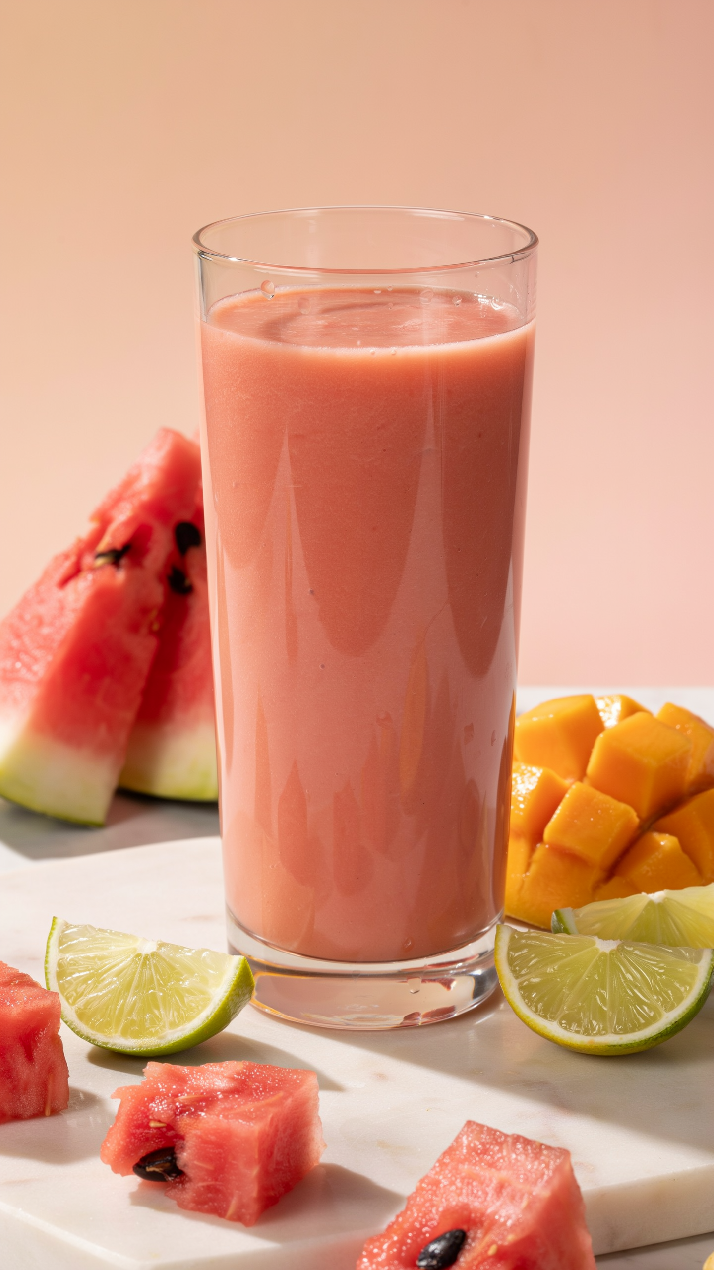 Watermelon mango lime smoothie for summer in a glass with tropical fruit and lime garnish
