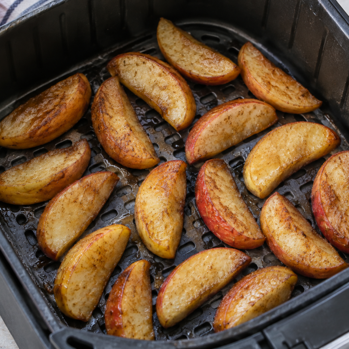 Skin-on cinnamon apple wedges with lightly browned edges arranged in a spaced single layer in an open air-fryer basket.