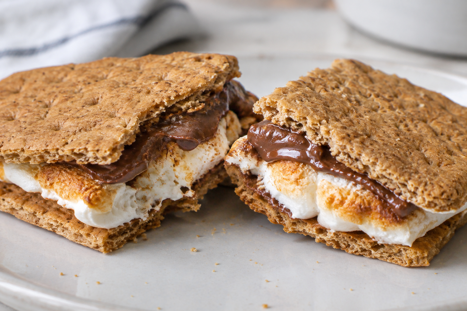 A s’more broken into two pieces reveals softened milk chocolate above gooey toasted marshmallow between graham crackers.