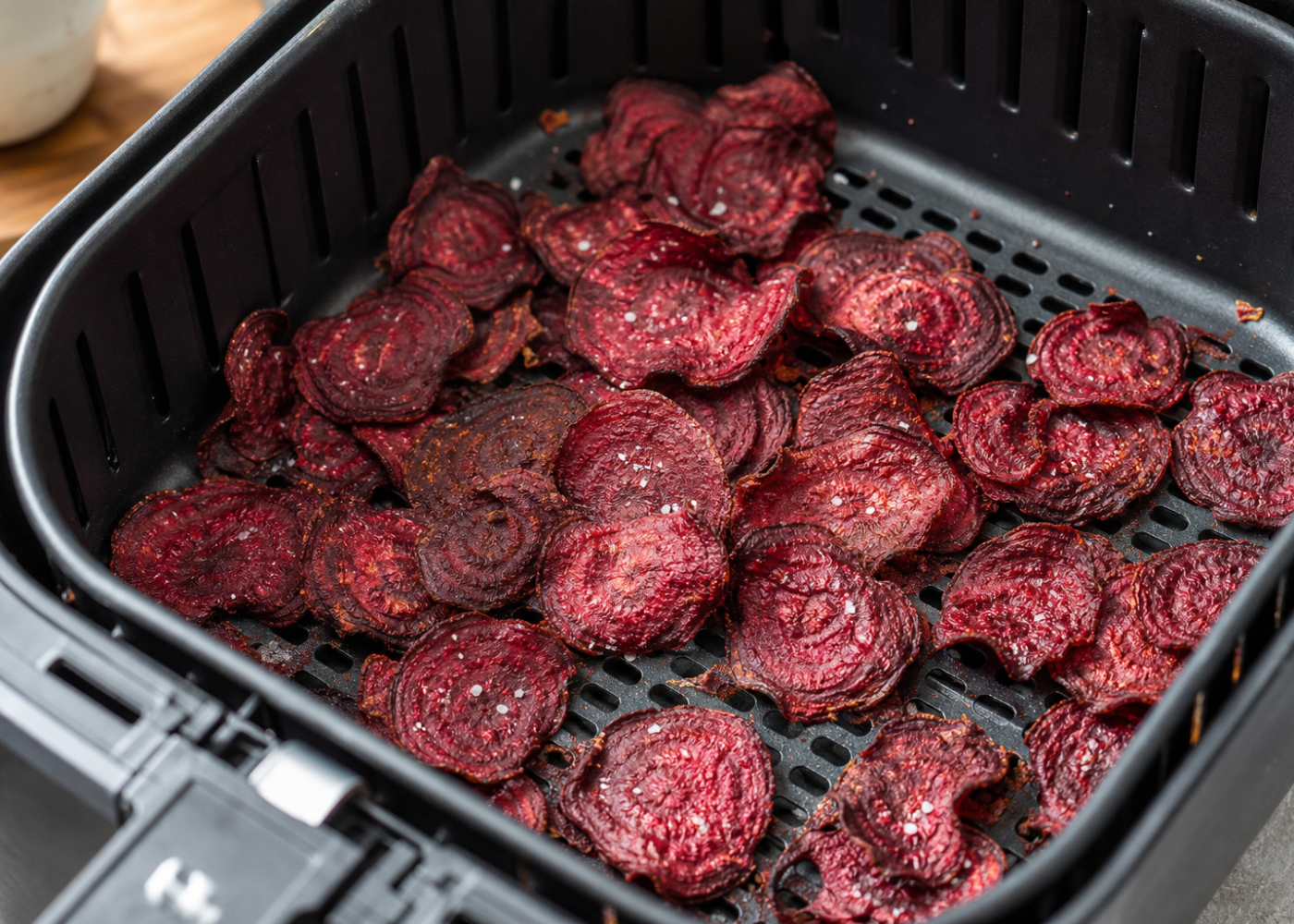 Thin, crispy sea-salted beet chips in an open air fryer basket with its perforated grid visible.