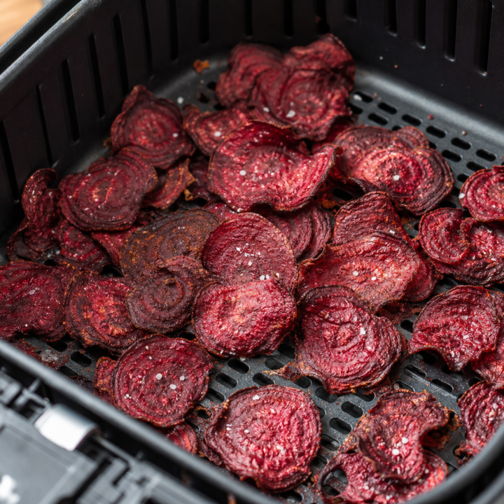 Thin, crispy sea-salted beet chips in an open air fryer basket with its perforated grid visible.