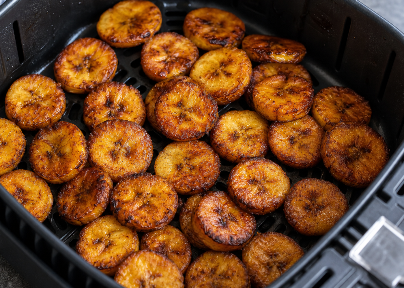 Golden sweet plantain slices filling an open air-fryer basket, with the perforated grid visible.